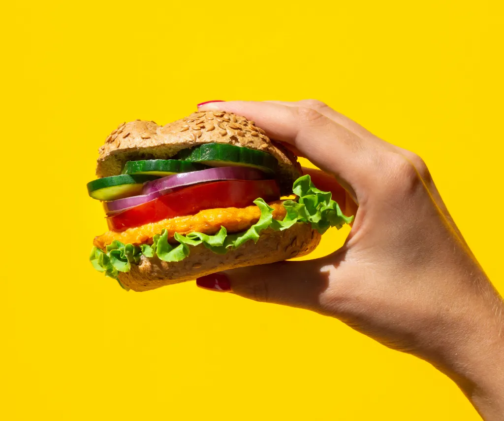 hand holding a burger on a yellow background