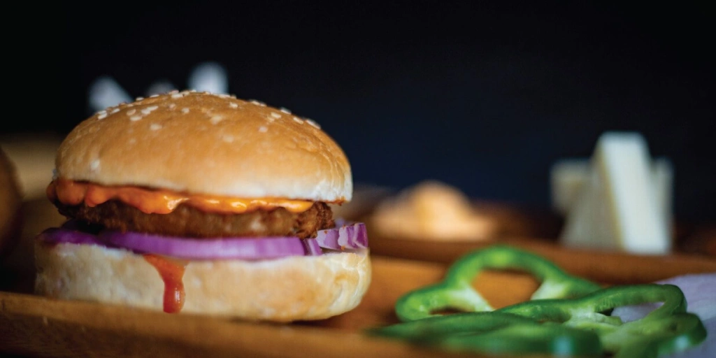 A burger made with a veggie patty with some mayonnaise and onions between the bun