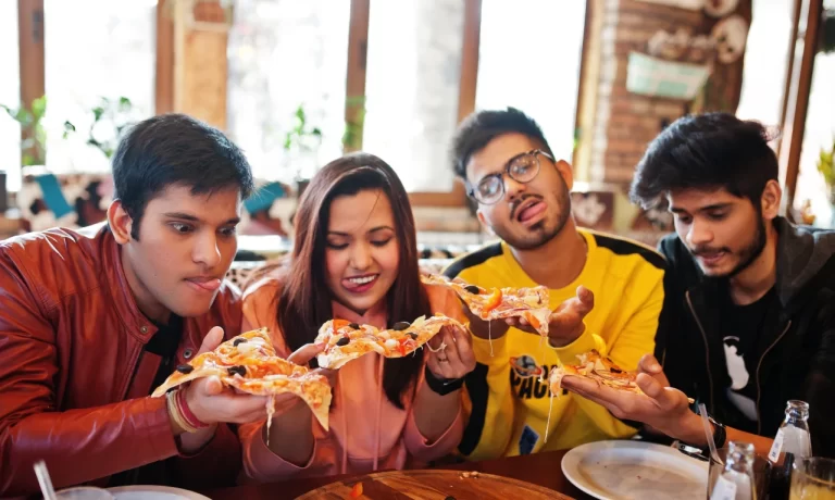 A group of Indian youngsters trying to eat a pizza at a cafe