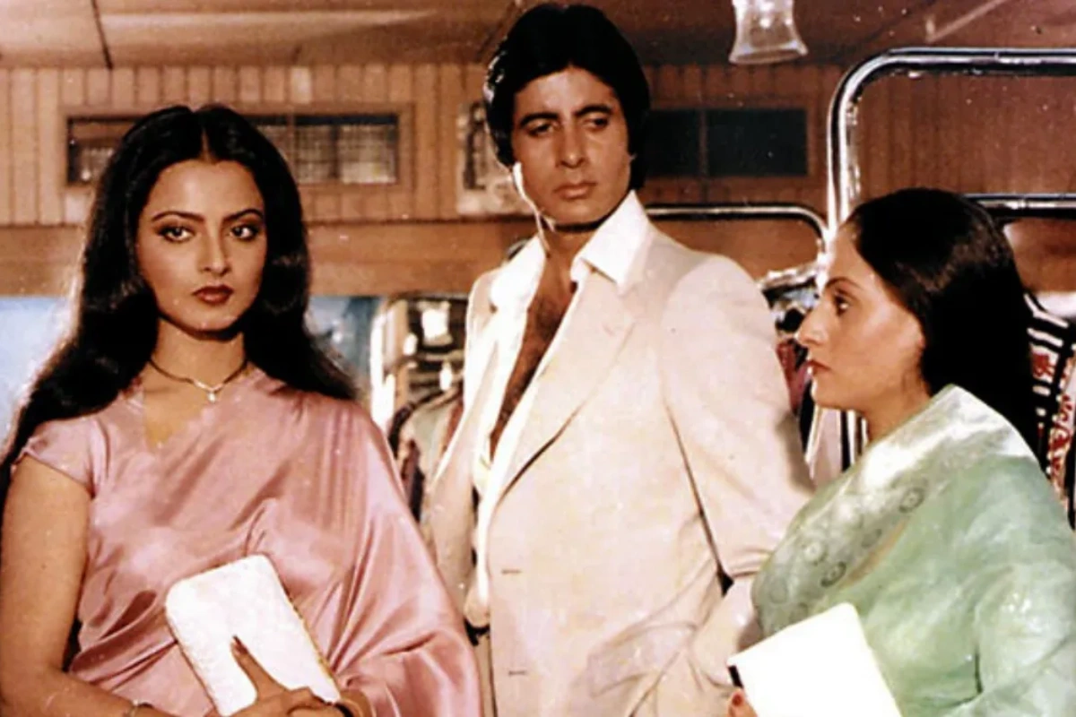 man in a suit and 2 women in saree are standing beside each other while the man is looking at one woman while ignoring the other.